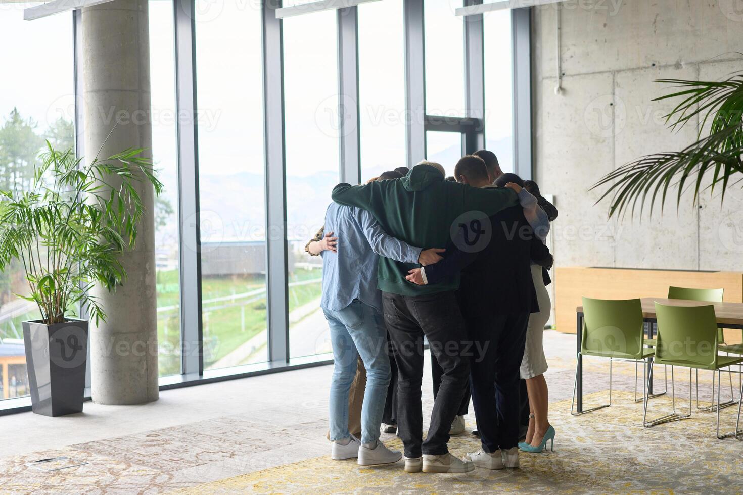 A diverse group of professionals standing in a supportive circle, embracing each other in a modern office space filled with natural light. photo