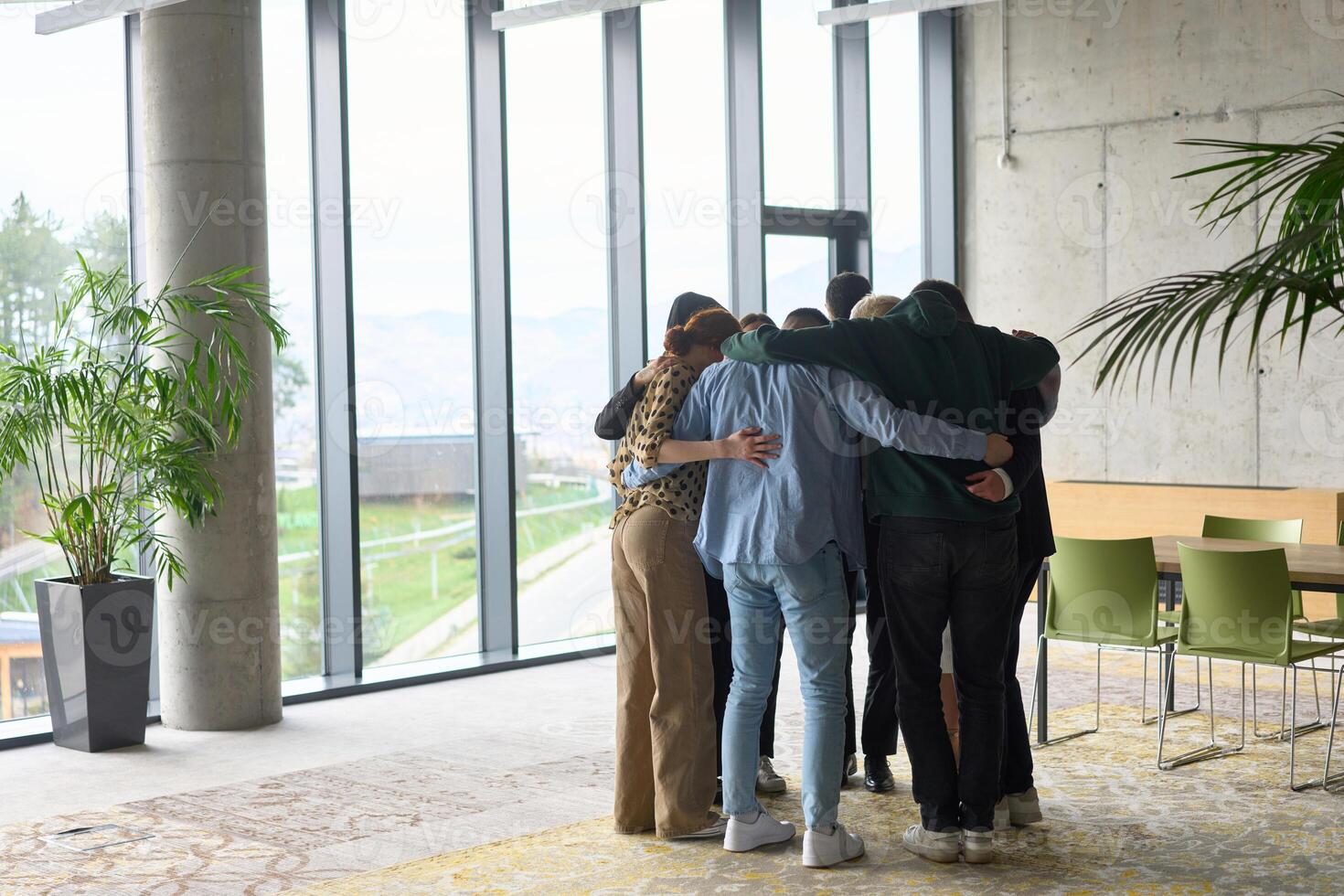 A diverse group of professionals standing in a supportive circle, embracing each other in a modern office space filled with natural light. photo