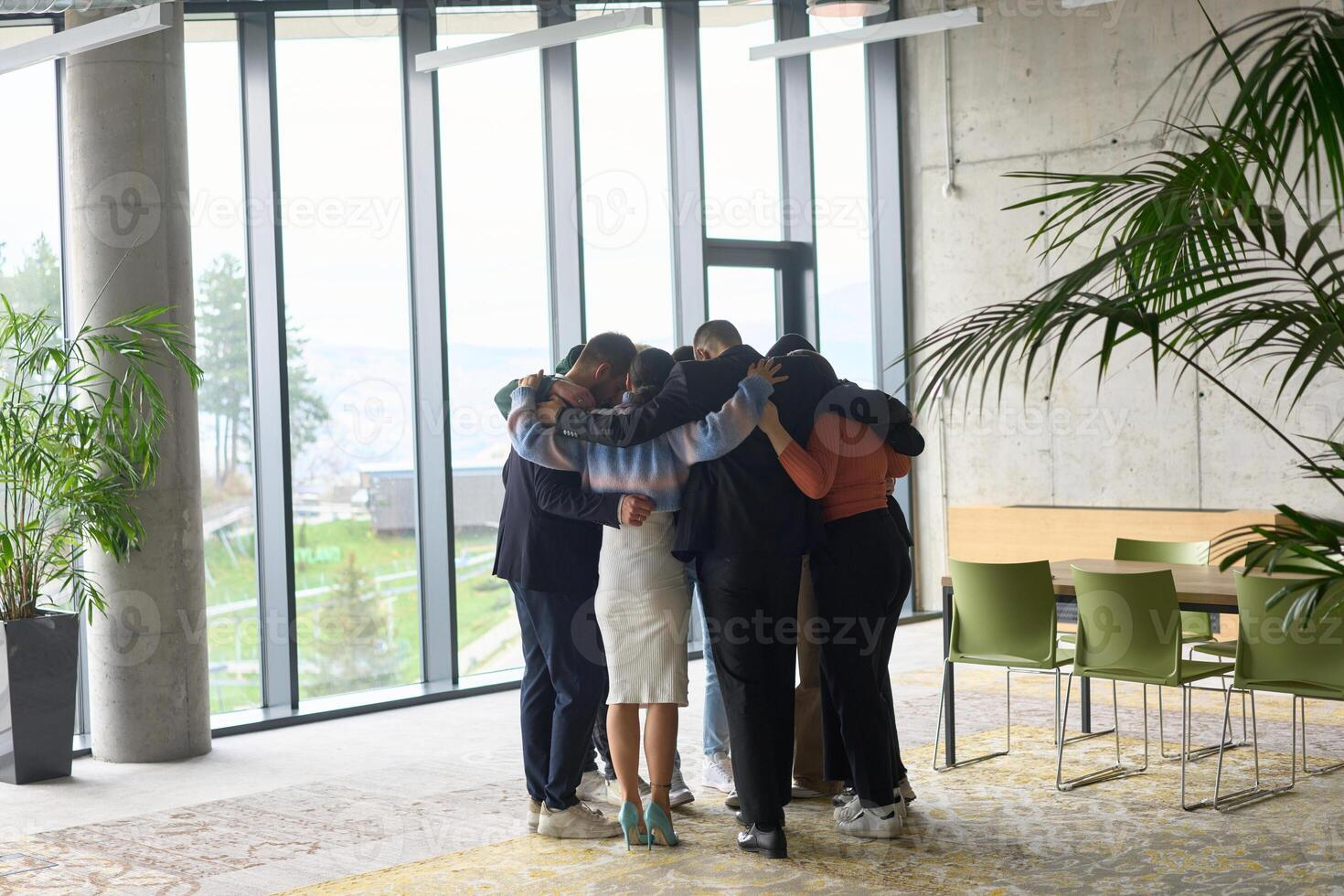 A diverse group of professionals standing in a supportive circle, embracing each other in a modern office space filled with natural light. photo