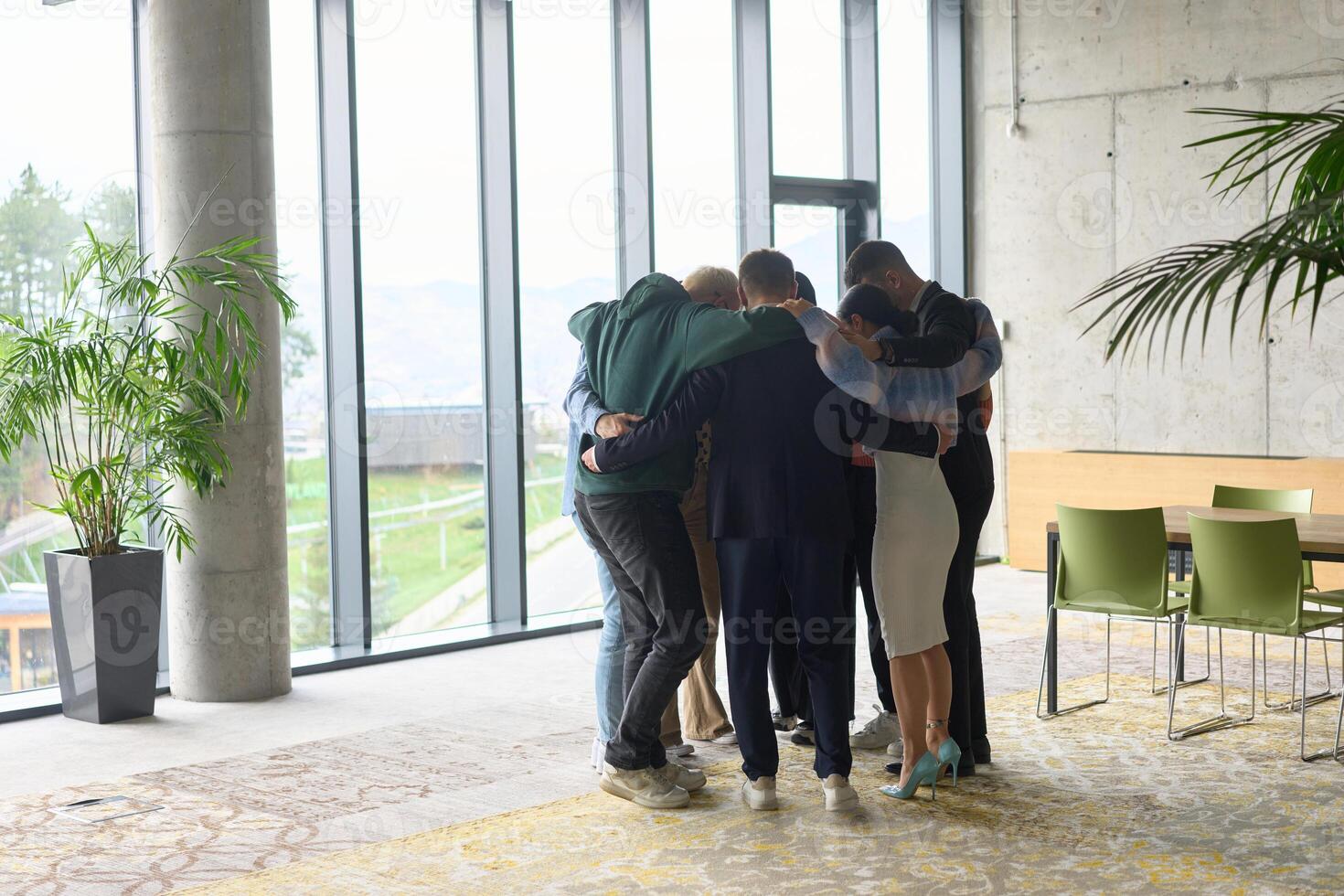 A diverse group of professionals standing in a supportive circle, embracing each other in a modern office space filled with natural light. photo