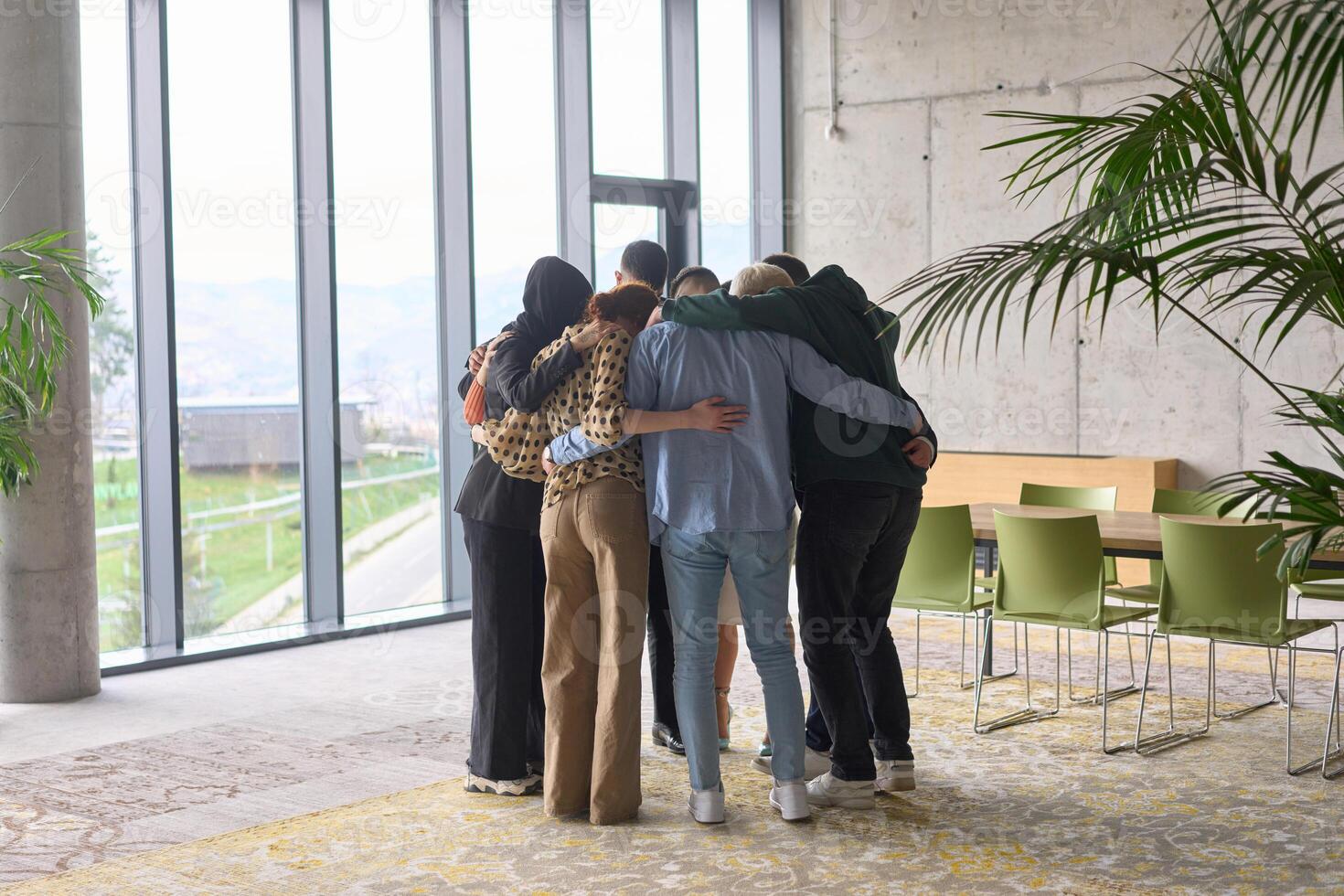 A diverse group of professionals standing in a supportive circle, embracing each other in a modern office space filled with natural light. photo