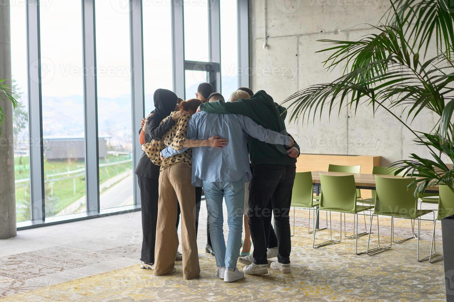 A diverse group of professionals standing in a supportive circle, embracing each other in a modern office space filled with natural light. photo
