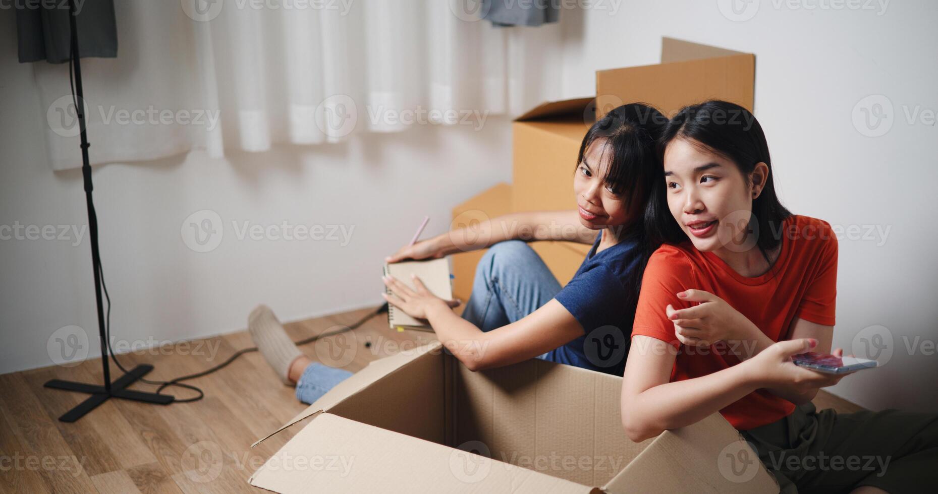 High angle view, Two young Asian women sit with backs to each other on the floor and discuss ideas for designing a room together in new home. Moving to a new home concept photo