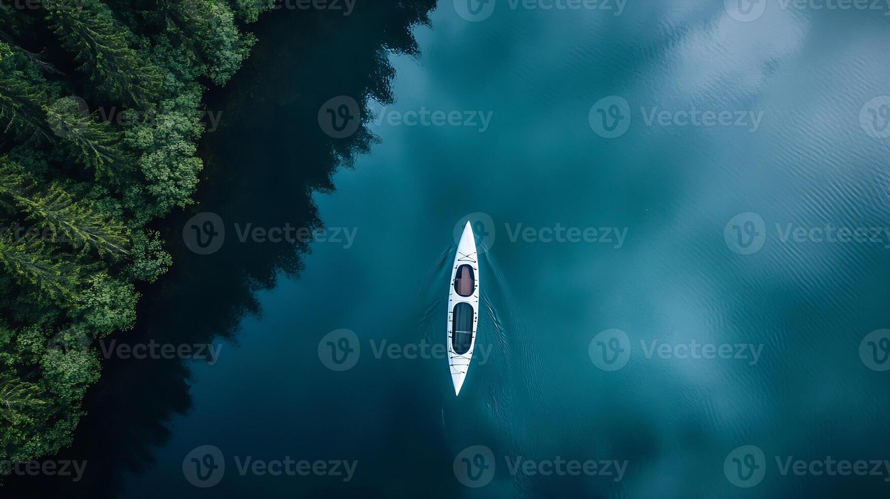 Serene aerial view of blue kayak paddling through forest-bordered tranquil lake photo