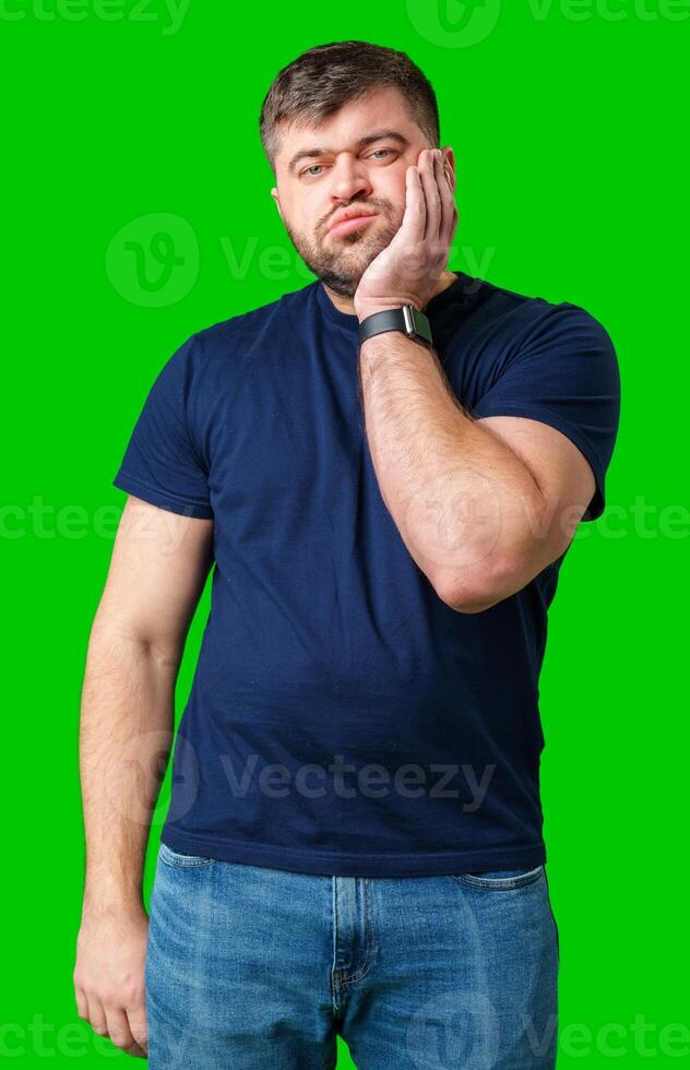 Young man with a contemplative expression leaning against green backdrop while resting his head on his hand photo
