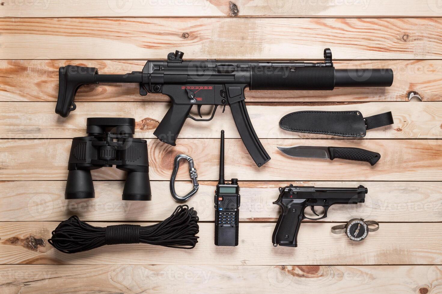 Assault rifle, gun, knife with sheath, compass and notebook with pen on table. photo