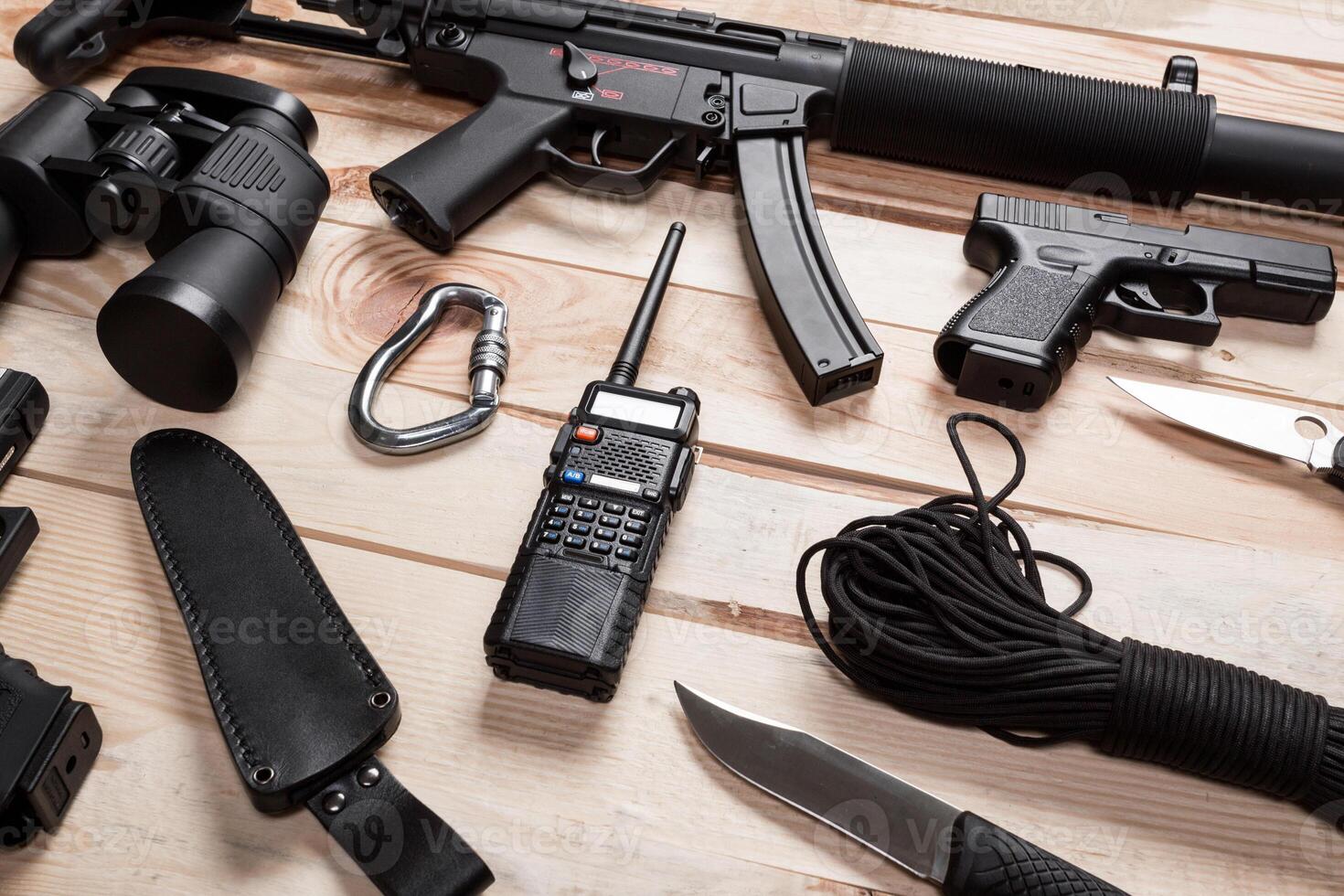 Assault rifle, gun, knife with sheath, compass and notebook with pen on table. photo