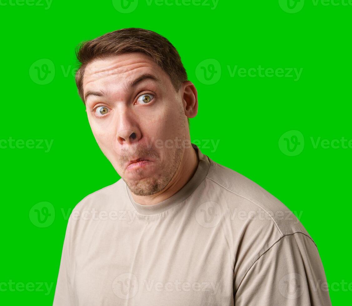 A surprised man stands in front of a bright green screen, expressing shock with his mouth open photo