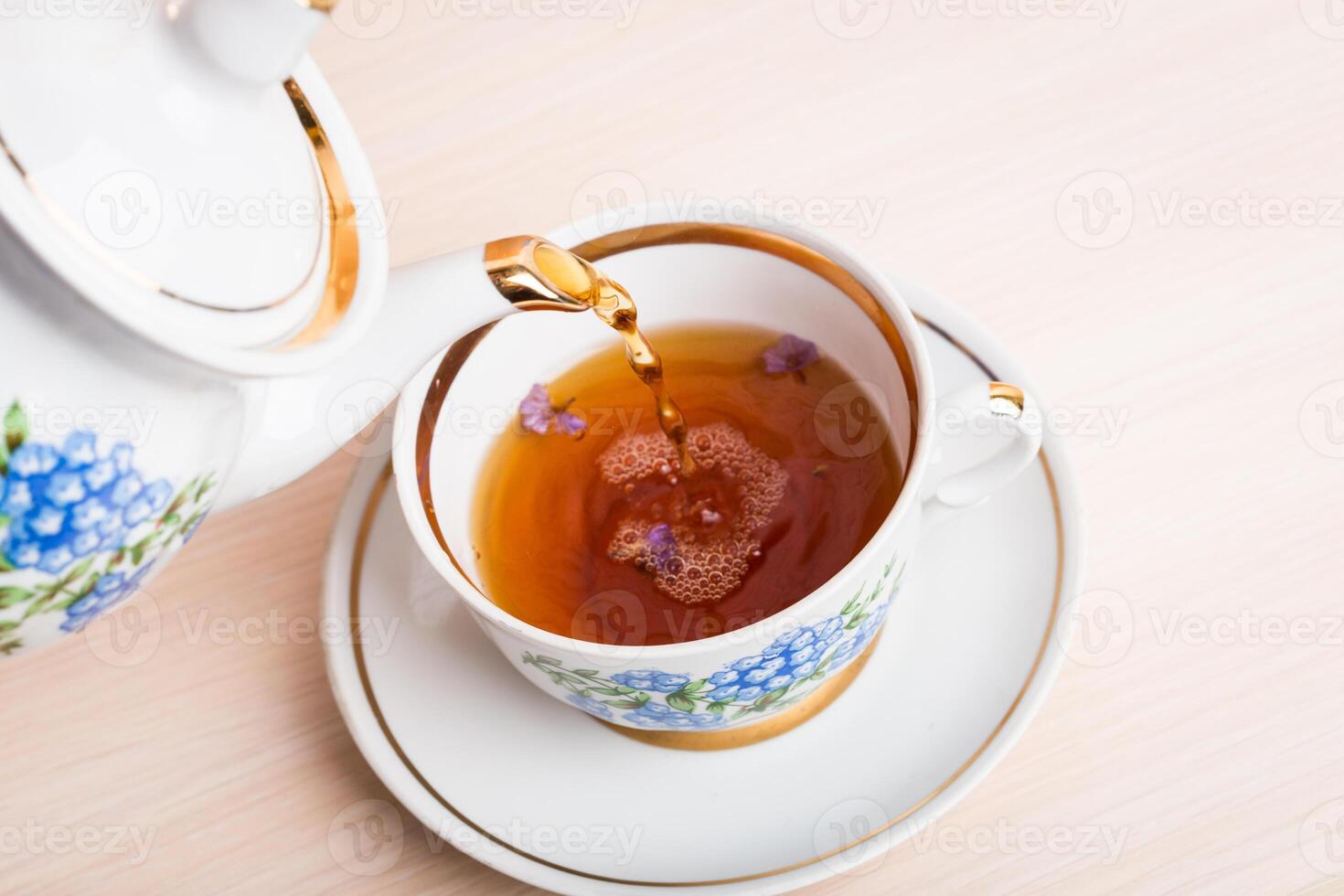 Old-style porcelain kettle pouring tea from jug to cup of tea photo