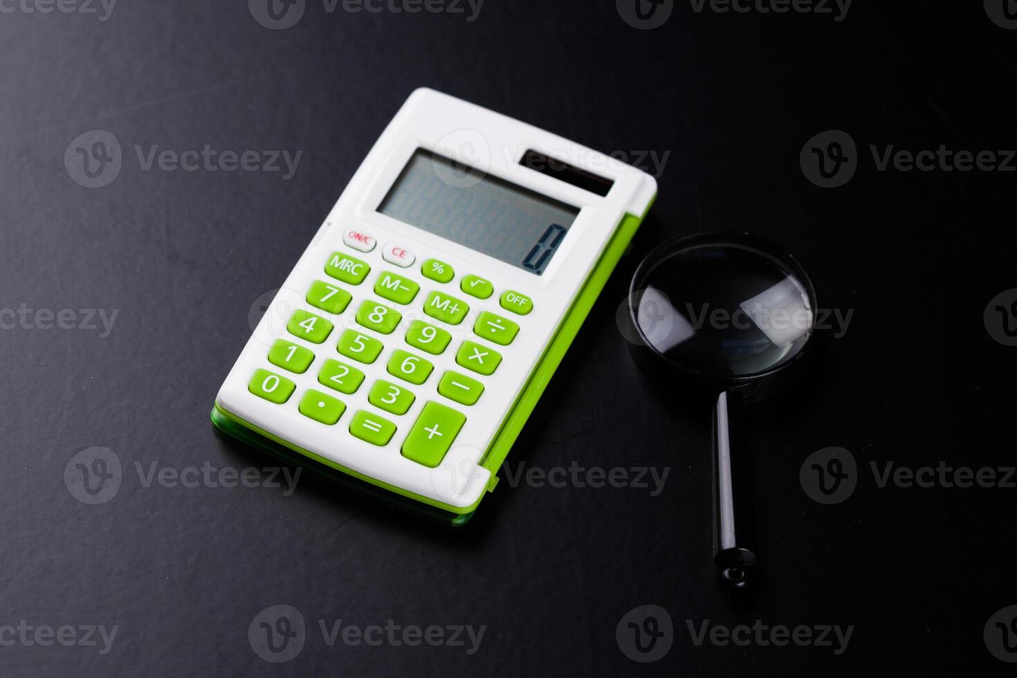 Calculator with a magnifying glass on a black background photo