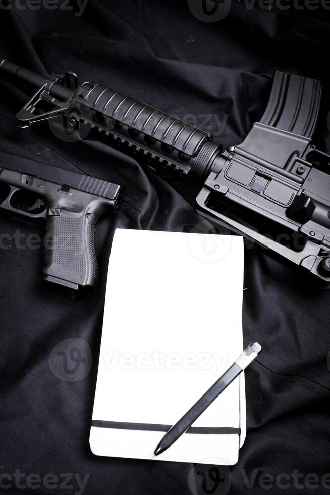 Rifle, gun, knife with sheath, compass and notebook with pen on on black cloth photo