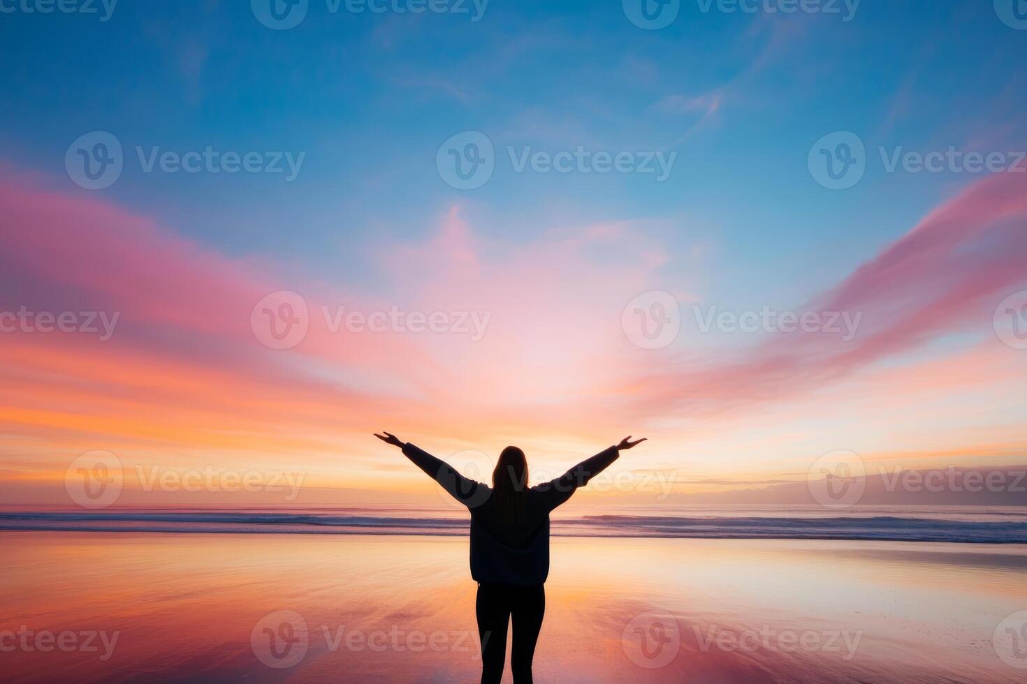 Silhouette of a person with outstretched arms enjoying a breathtaking sunset at the beach during twilight hours photo