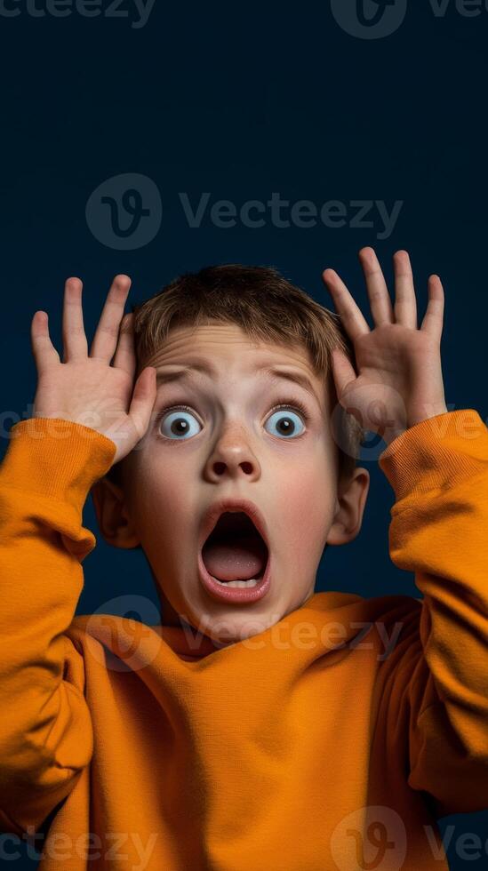 A young boy expresses surprise with wide eyes and an open mouth, raising his hands in an exaggerated manner against a dark background photo