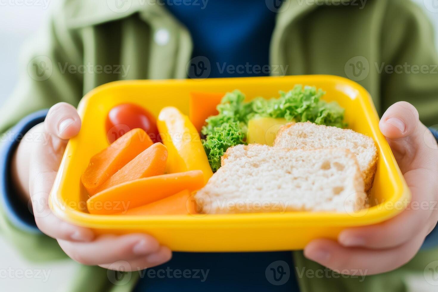 A child holds a vibrant lunchbox filled with vegetables, fruits, and bread in a bright setting at school during midday photo