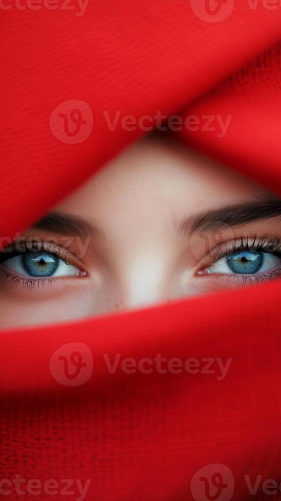 A close-up view of mesmerizing blue eyes partially covered with a vibrant red scarf in a serene indoor setting photo