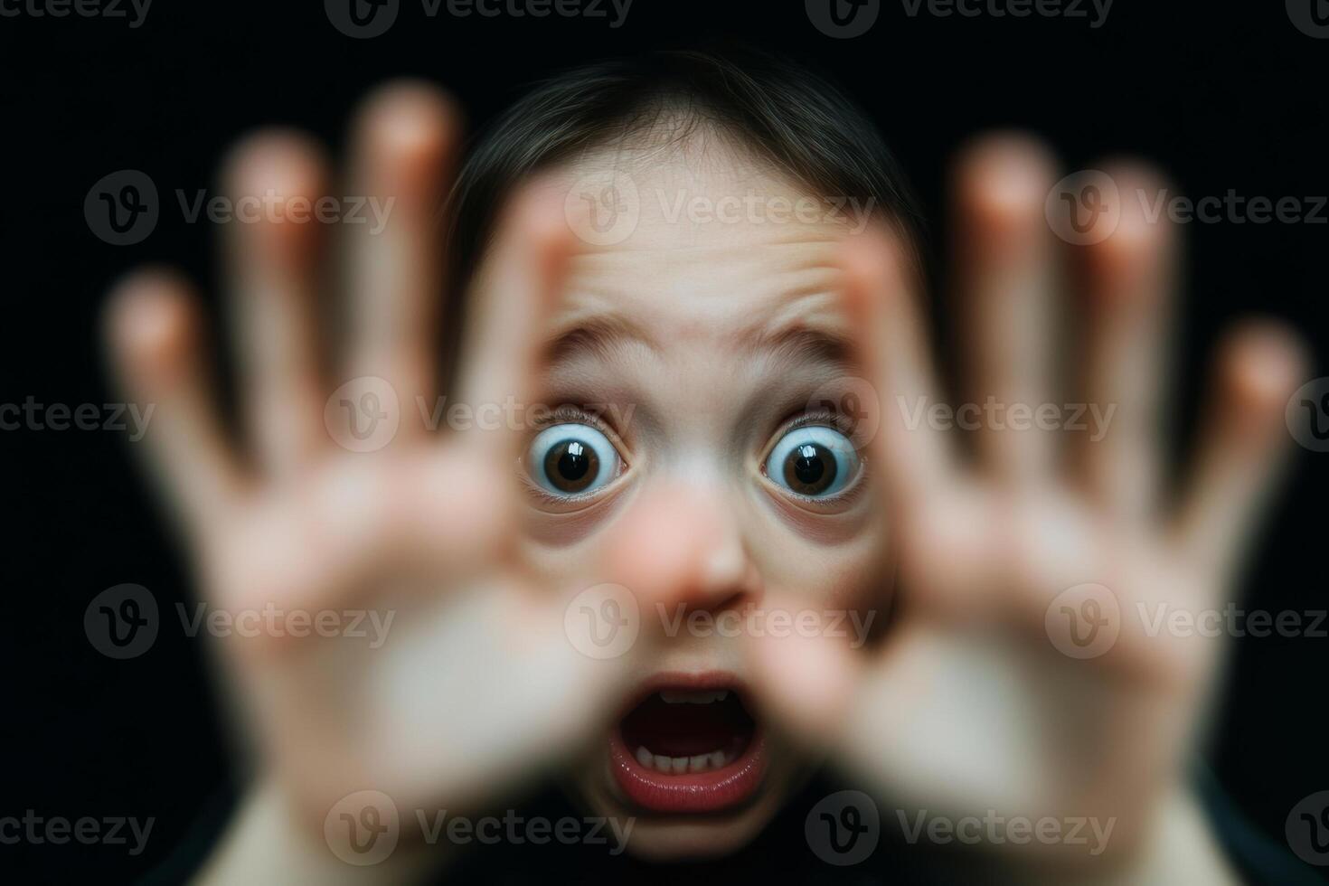 A young child expresses fear and surprise with wide eyes and outstretched hands against a black background photo