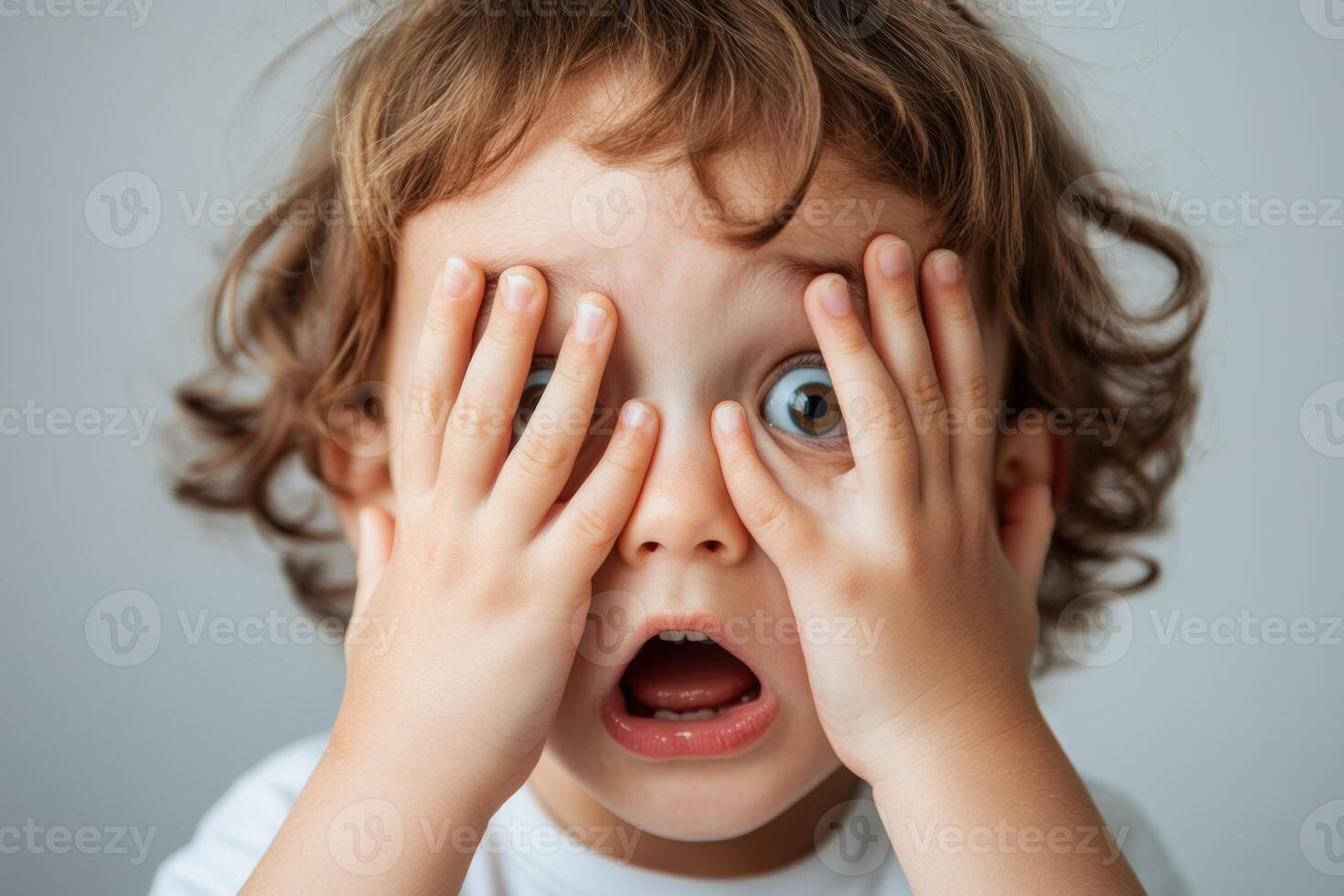 A young child covering their face in surprise while expressing strong emotions, captured indoors with a simple background photo