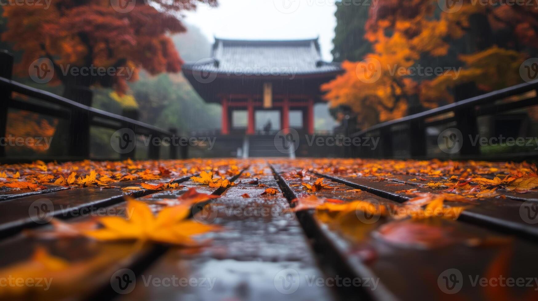 Vibrant autumn leaves blanket the wooden walkway leading to a traditional temple amidst a misty landscape in a serene setting photo