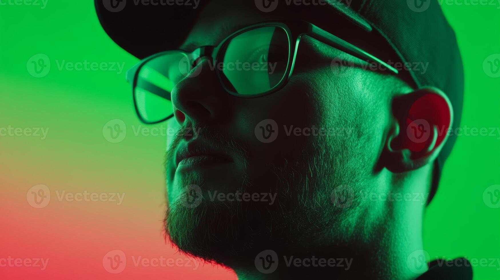 Young man with glasses in studio setting illuminated by vibrant green and red lights photo