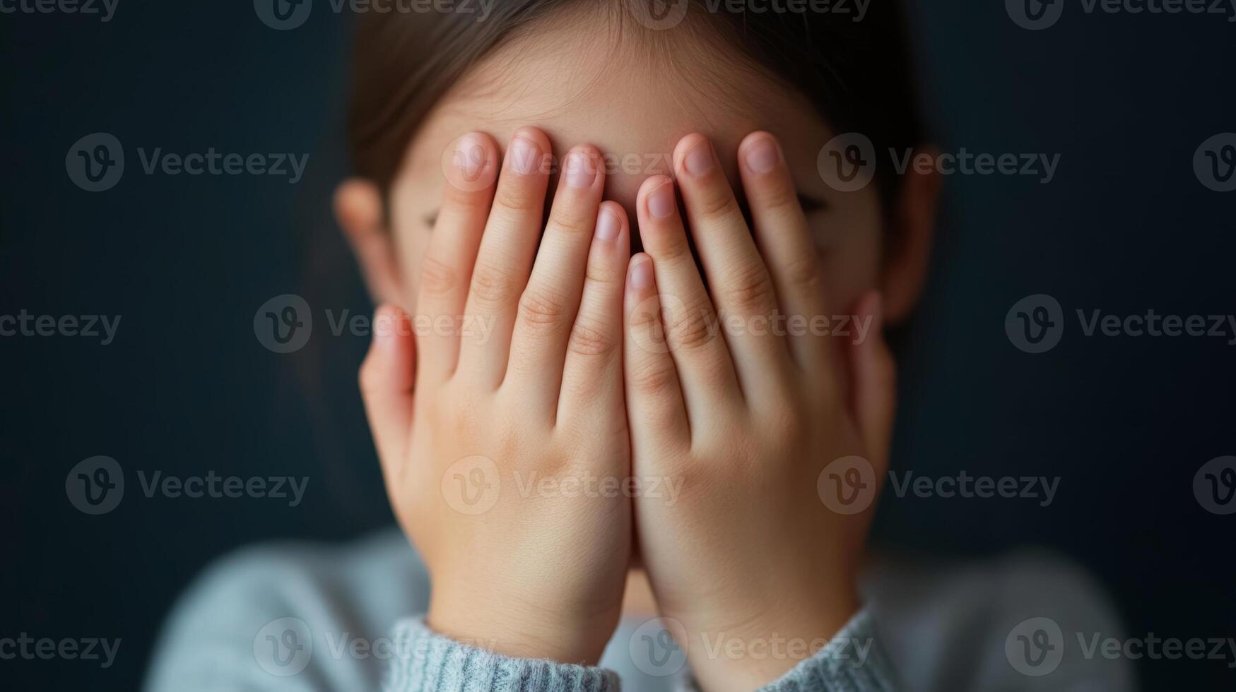 A young child playfully covering their face with both hands, expressing a sense of shyness or hide-and-seek joy in a cozy indoor setting photo