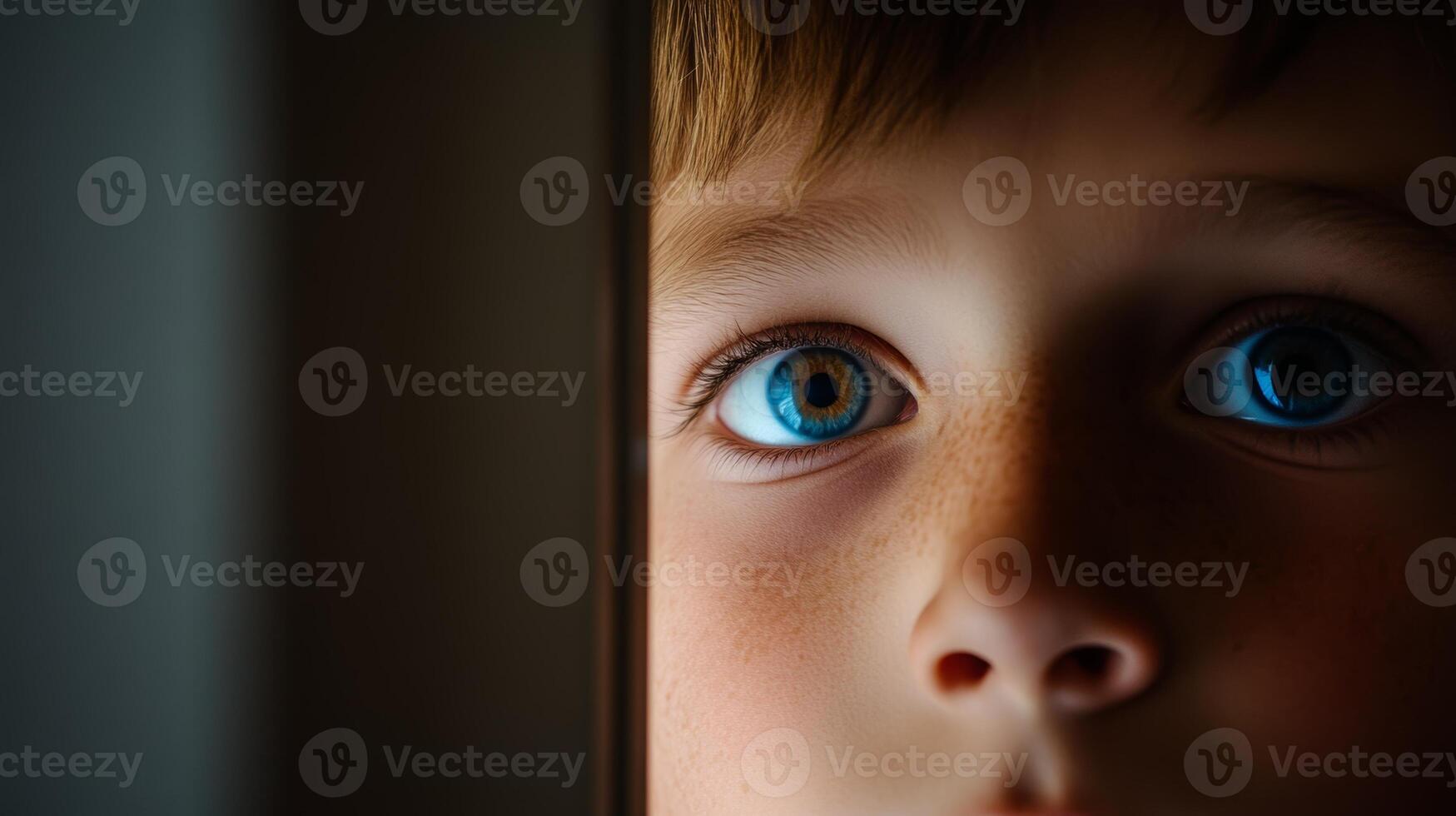 A young boy curiously peering through a slightly ajar door in a dimly lit room photo