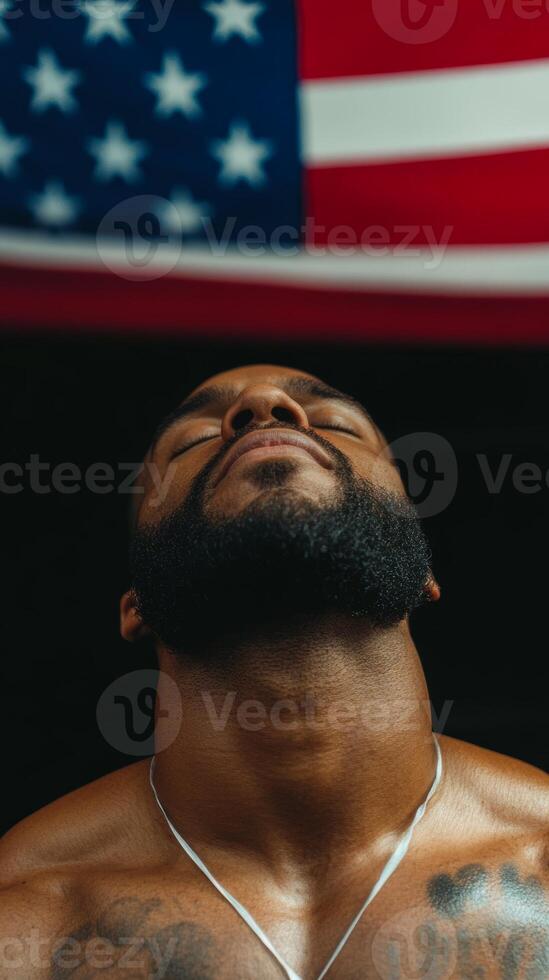A man with a beard gazing upward under an American flag in a gym, reflecting determination and strength during a workout session photo