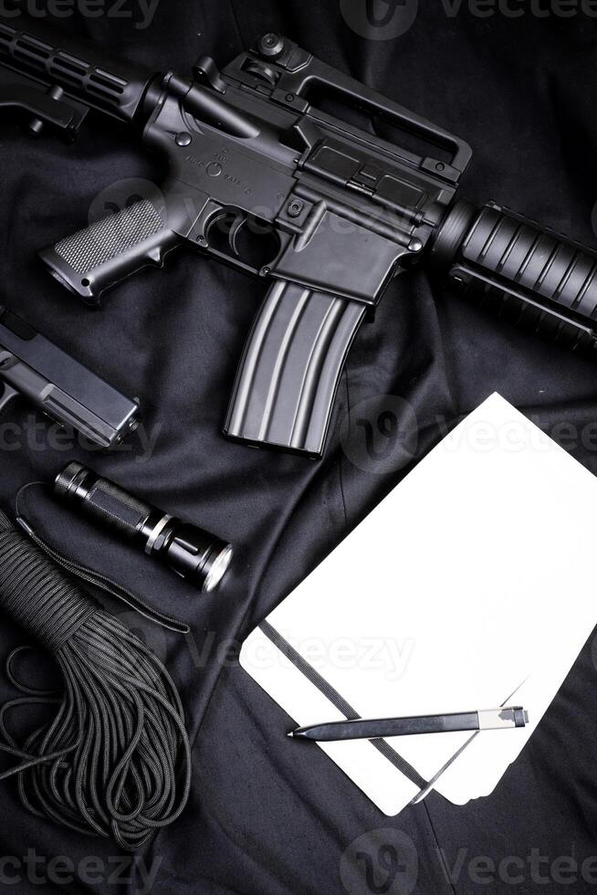 Rifle, gun, knife with sheath, compass and notebook with pen on on black cloth photo