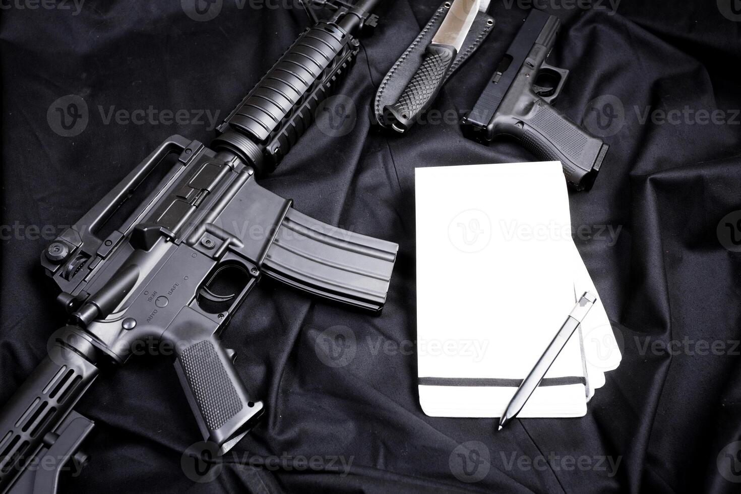 Rifle, gun, knife with sheath, compass and notebook with pen on on black cloth photo