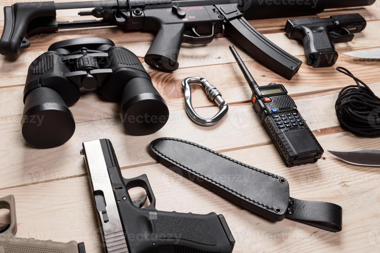 Assault rifle, gun, knife with sheath, compass and notebook with pen on table. photo