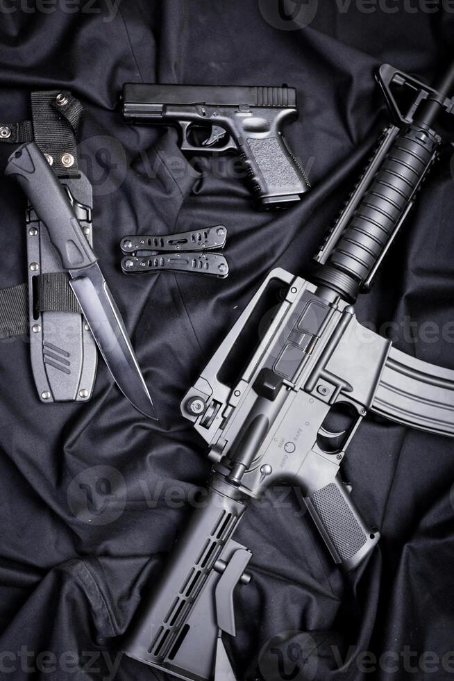 Rifle, gun, knife with sheath, compass and notebook with pen on on black cloth photo