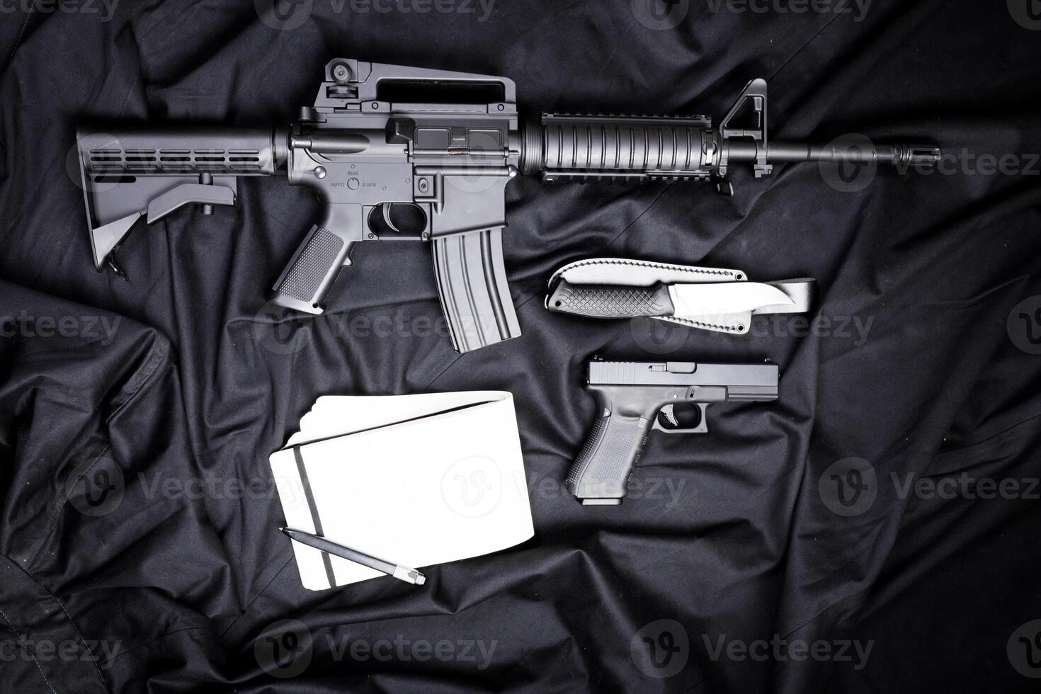 Rifle, gun, knife with sheath, compass and notebook with pen on on black cloth photo