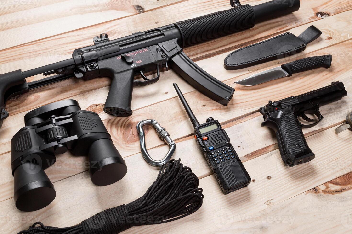 Assault rifle, gun, knife with sheath, compass and notebook with pen on table. photo