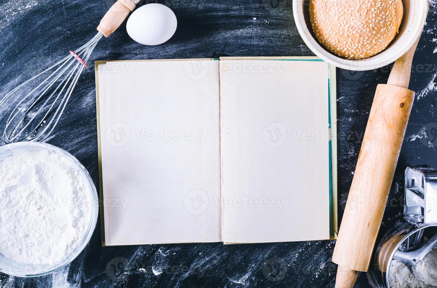 Baking dark background with blank cook book, eggshell, bread, flour, rolling pin. Ingredients for the baking. photo