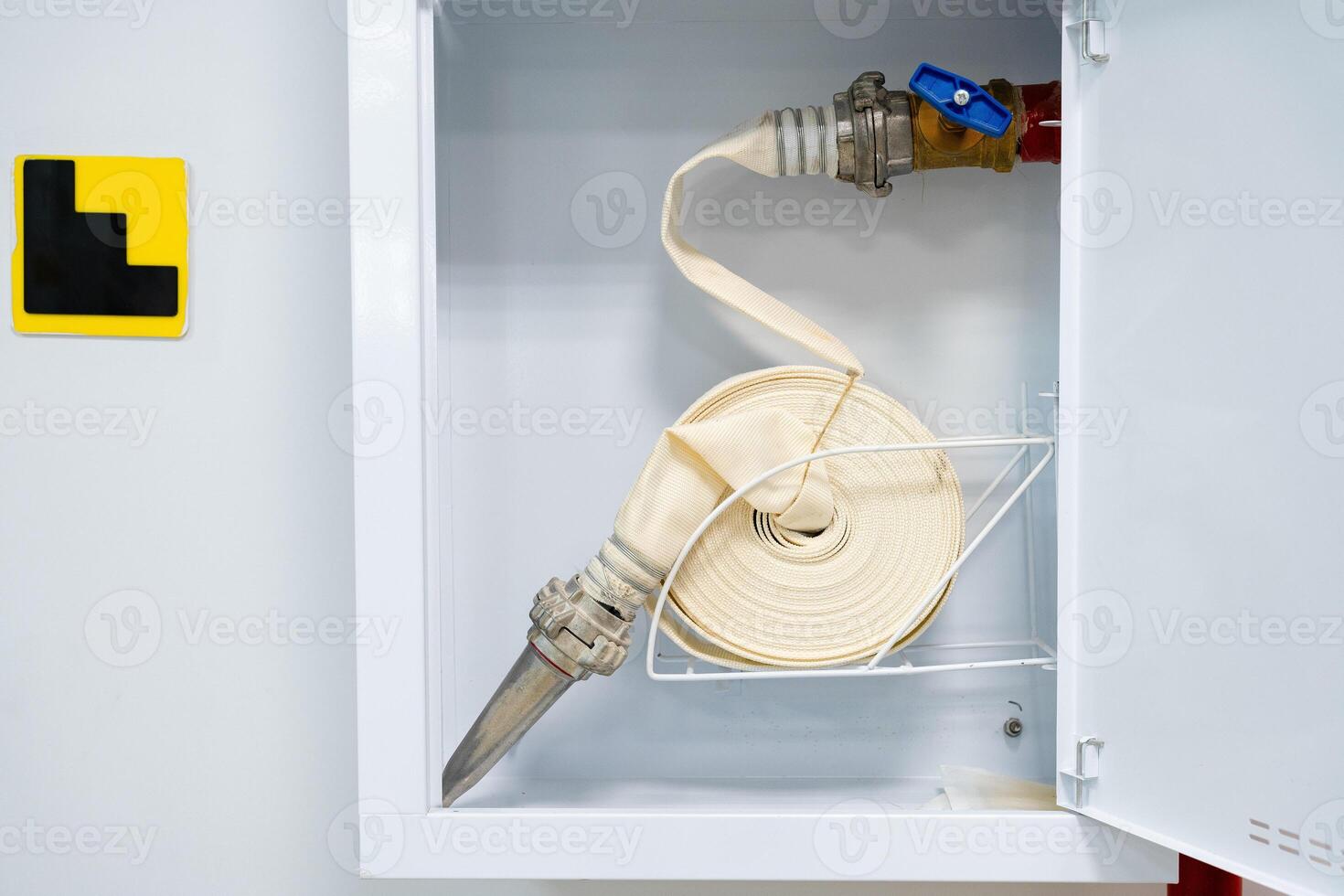 Fire hose in storage cabinet ready for emergency use with safety markings nearby photo