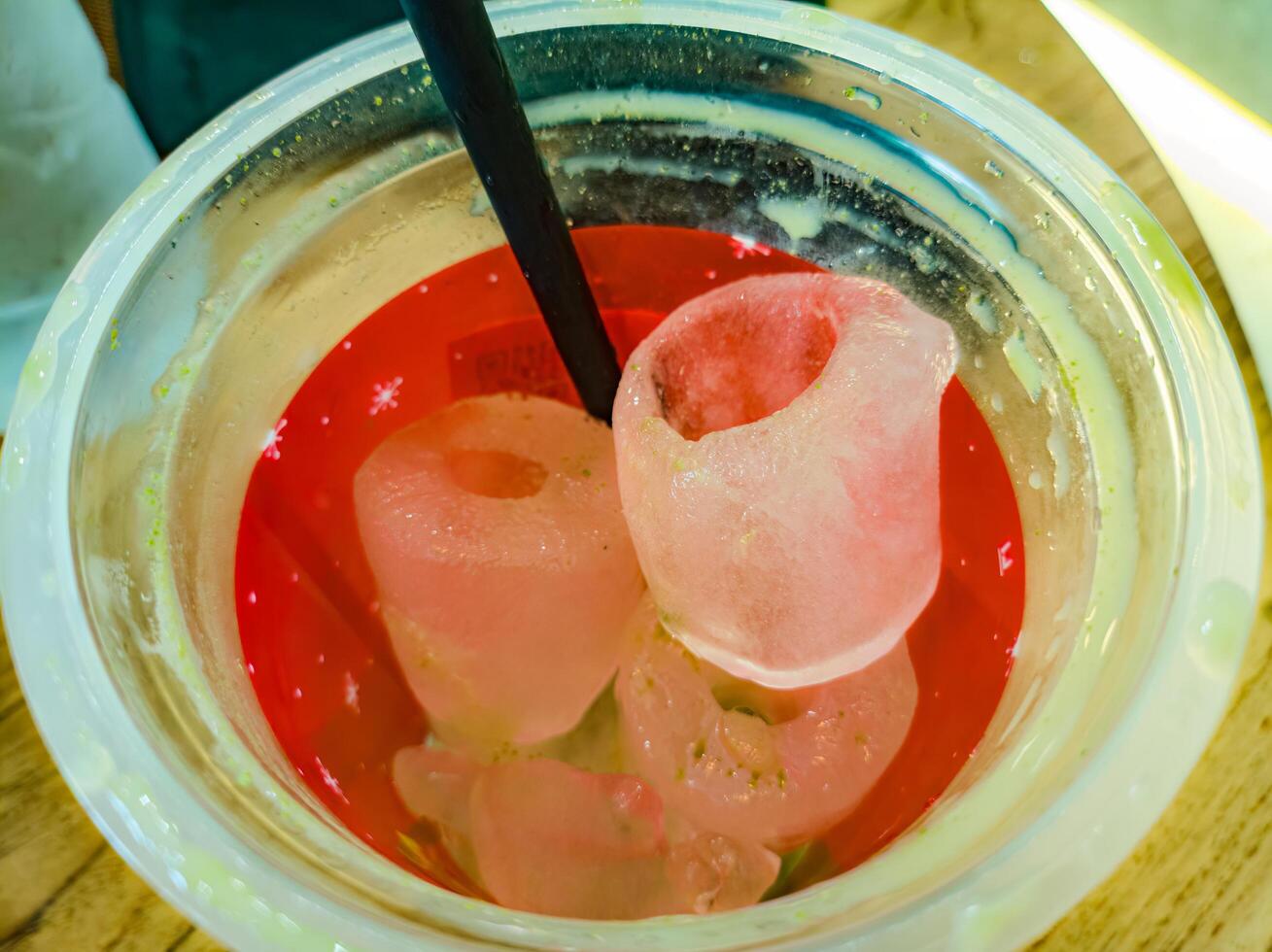 A close up of a red beverage in a plastic cup with large, hollow ice cubes and a black straw. The ice cubes have a unique, cylindrical shape, making the drink visually appealing photo