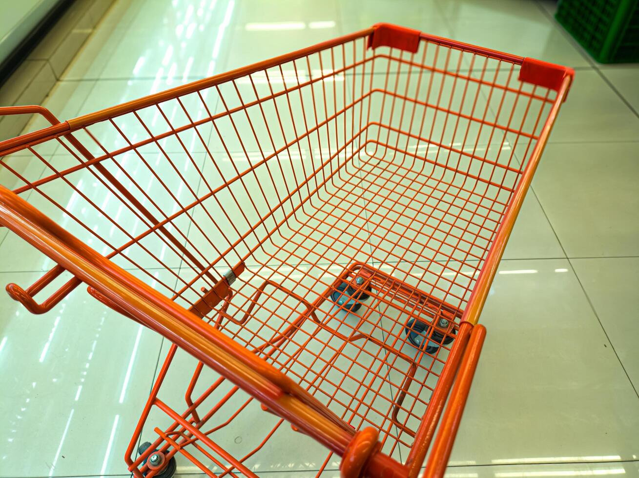 An empty orange shopping cart with a wireframe design is seen in a brightly lit supermarket aisle, ready for use photo