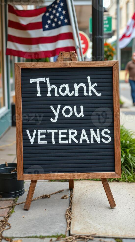 Sign expressing gratitude for veterans displayed on sidewalk with American flags in background photo