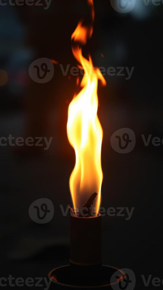 Fire burning brightly from a torch on a dark night under a subtle glow of distant lights photo