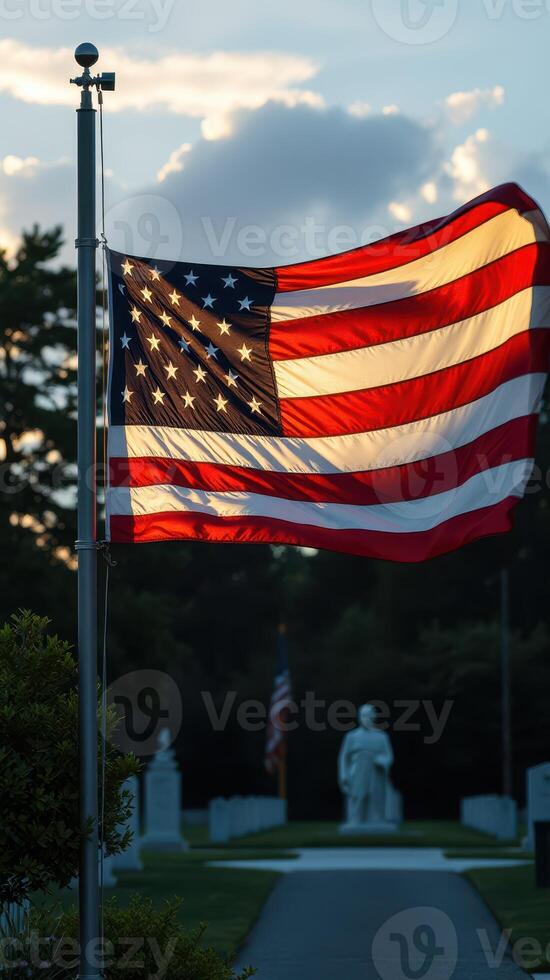 American flag waves proudly in evening light near memorial statues in a serene cemetery setting photo