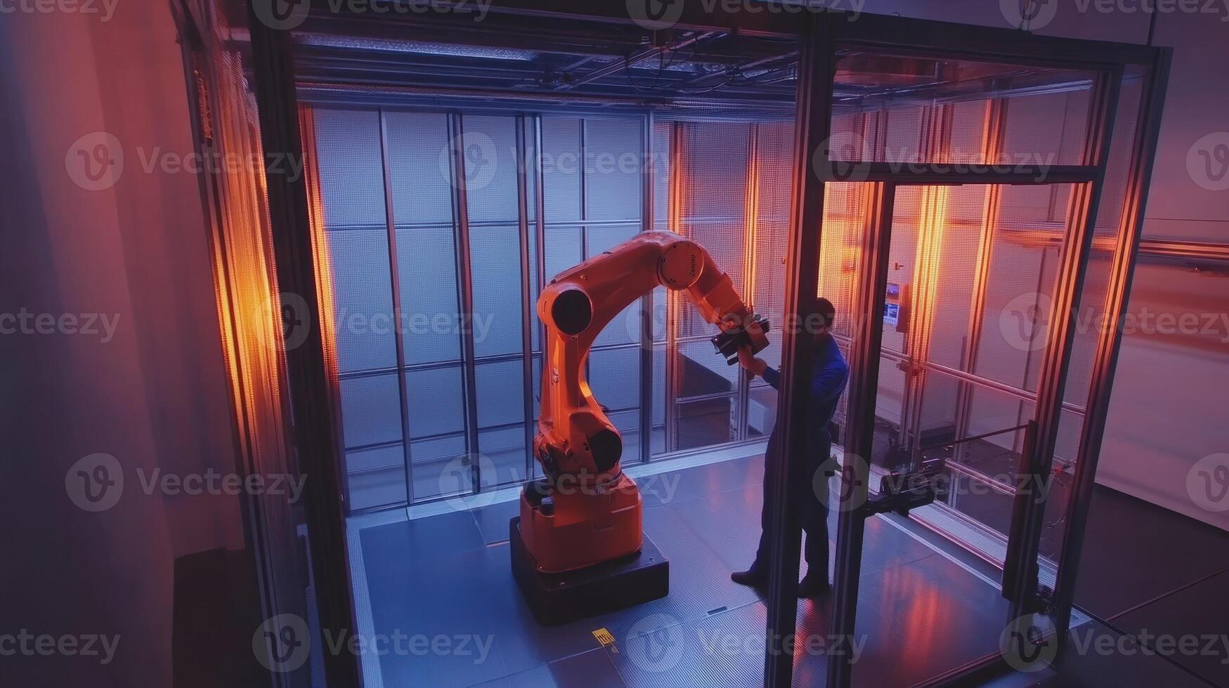 Engineer working with industrial robotic arm inside transparent cage photo
