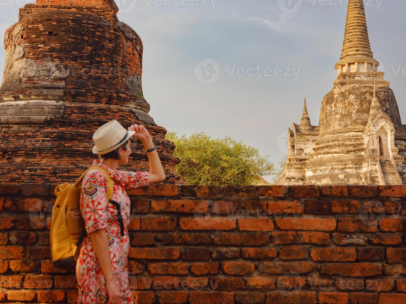 Young female tourist in dress exploring historic park of Ayutthaya, Thailand. Wat Phra Si Sanphet ancient temples and statues, she enjoys peaceful atmosphere and rich cultural heritage. photo