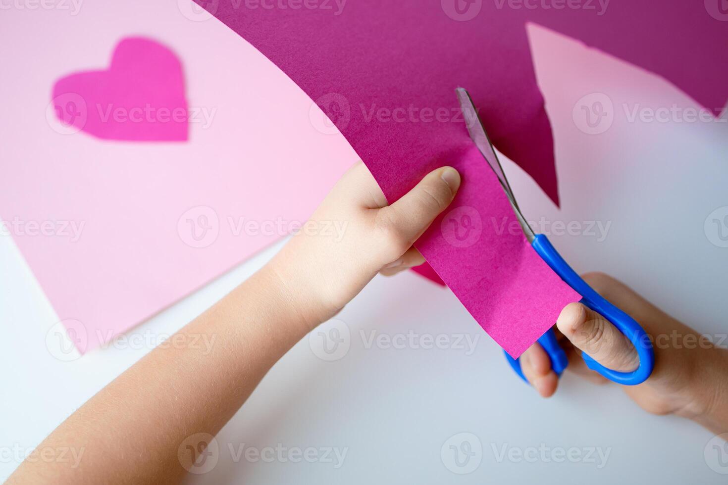 Child crafting. Hands cutting pink paper with scissors for heart art project photo
