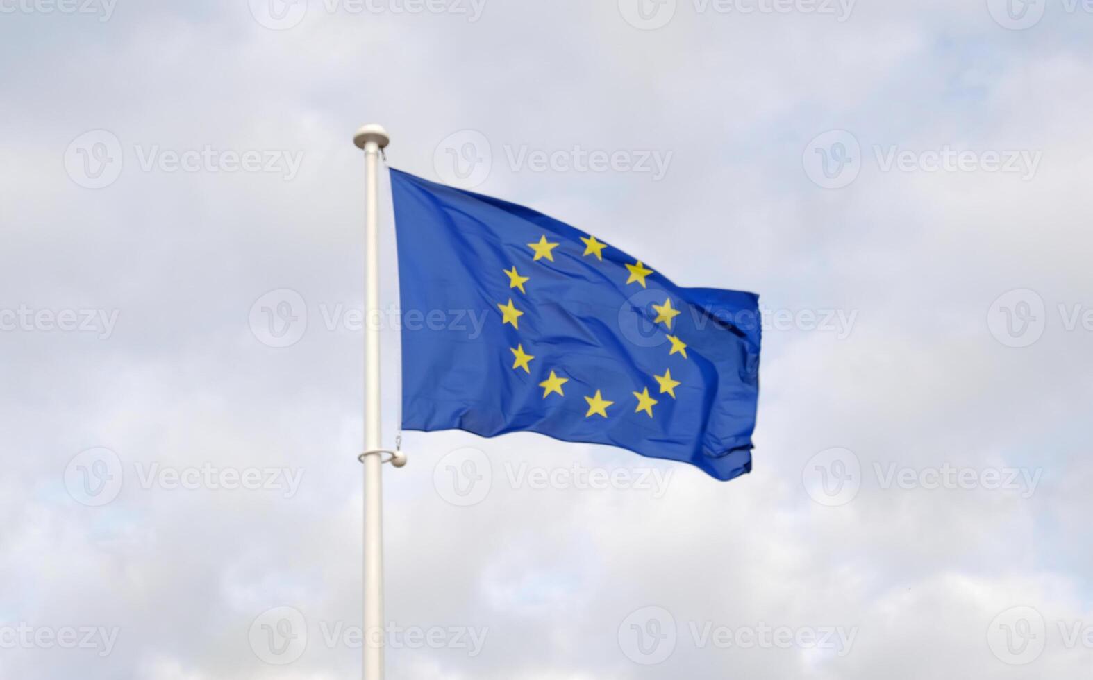 Flag of the European Union waving in the wind on flagpole against the blue sky. Close-up of single european flag with twelve yellow stars arranged in a circle. photo