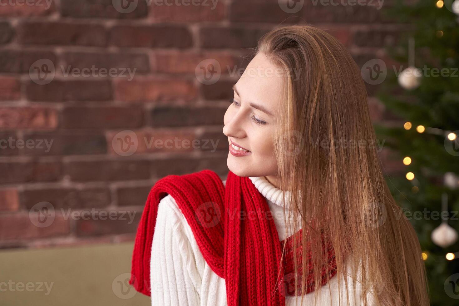 Caucasian young woman in festive red scarf smiling near decorated christmas tree indoors. photo