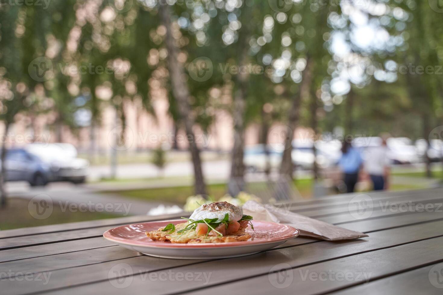 Delicious plate of eggs benedict with fresh arugula on an outdoor table in a sunny park setting. photo