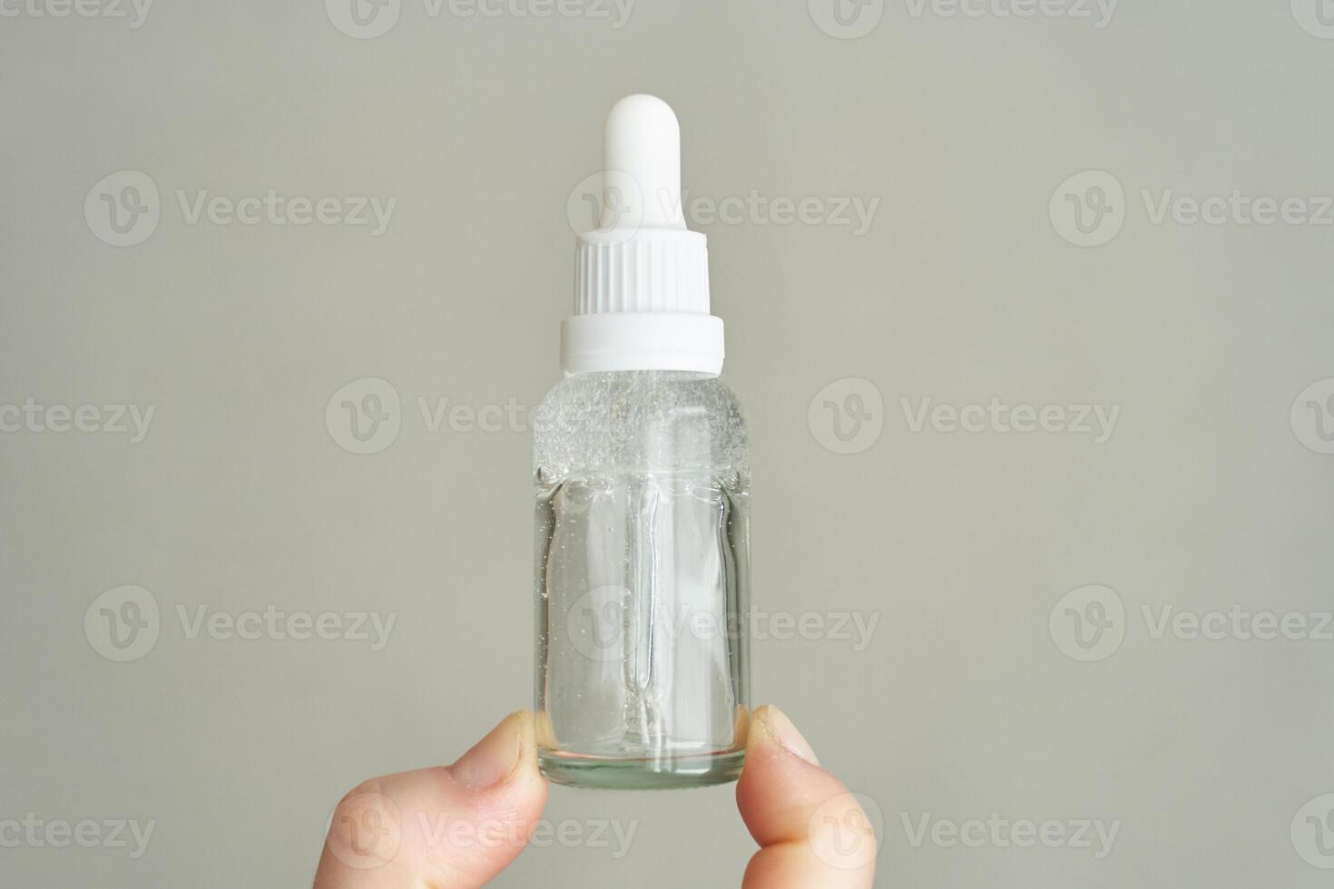 Hand holding glass dropper bottle with clear liquid for skincare or aromatherapy. photo