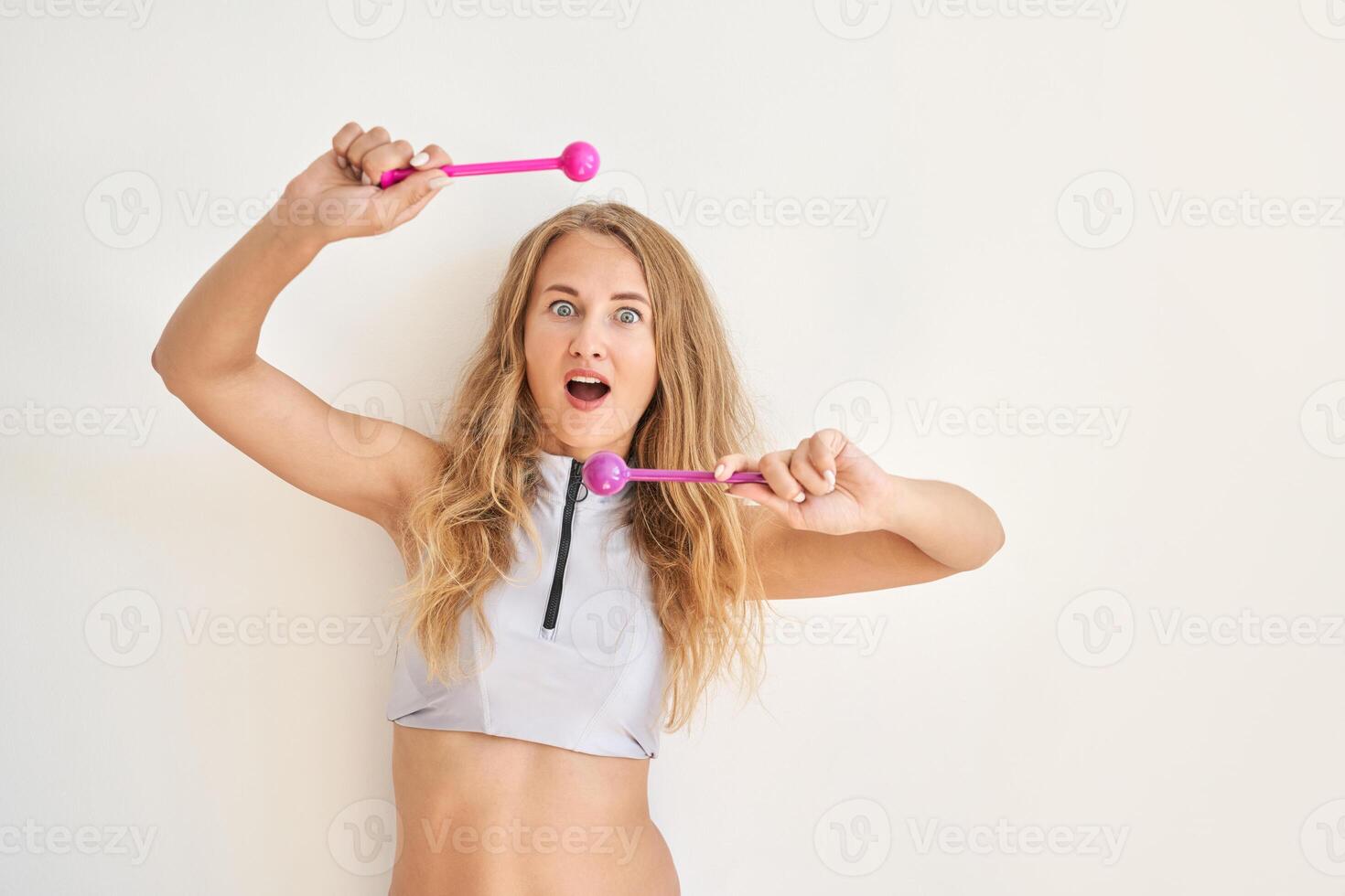 Young caucasian female playing with pink drumsticks in excitement against simple background. photo
