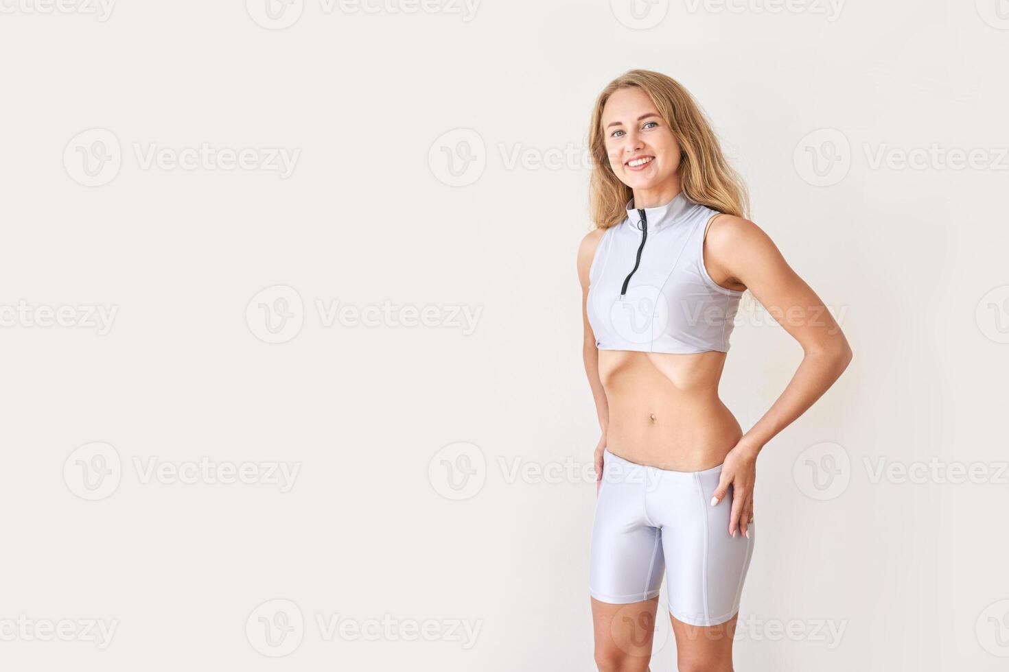 Young caucasian female in athletic wear smiling confidently against a minimalist background. photo