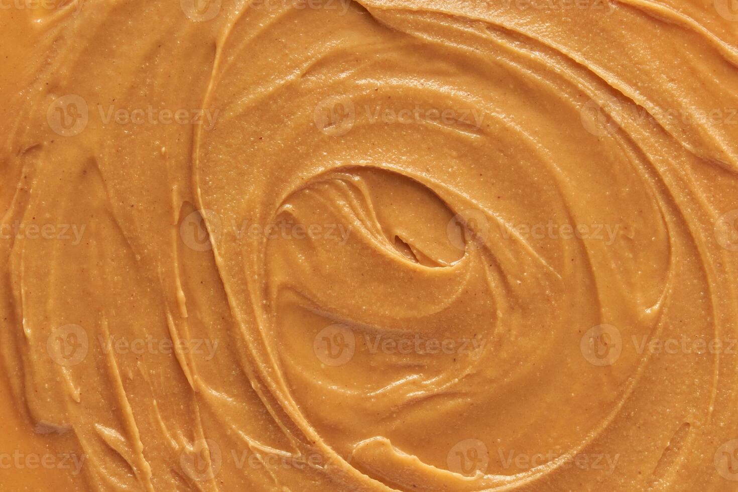 Smooth creamy peanut butter texture with swirls and rich nutty color close up view. photo
