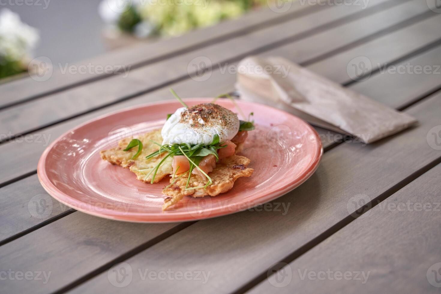 Delicious avocado and smoked salmon breakfast with poached egg on crisp hash browns on outdoor wooden table. photo